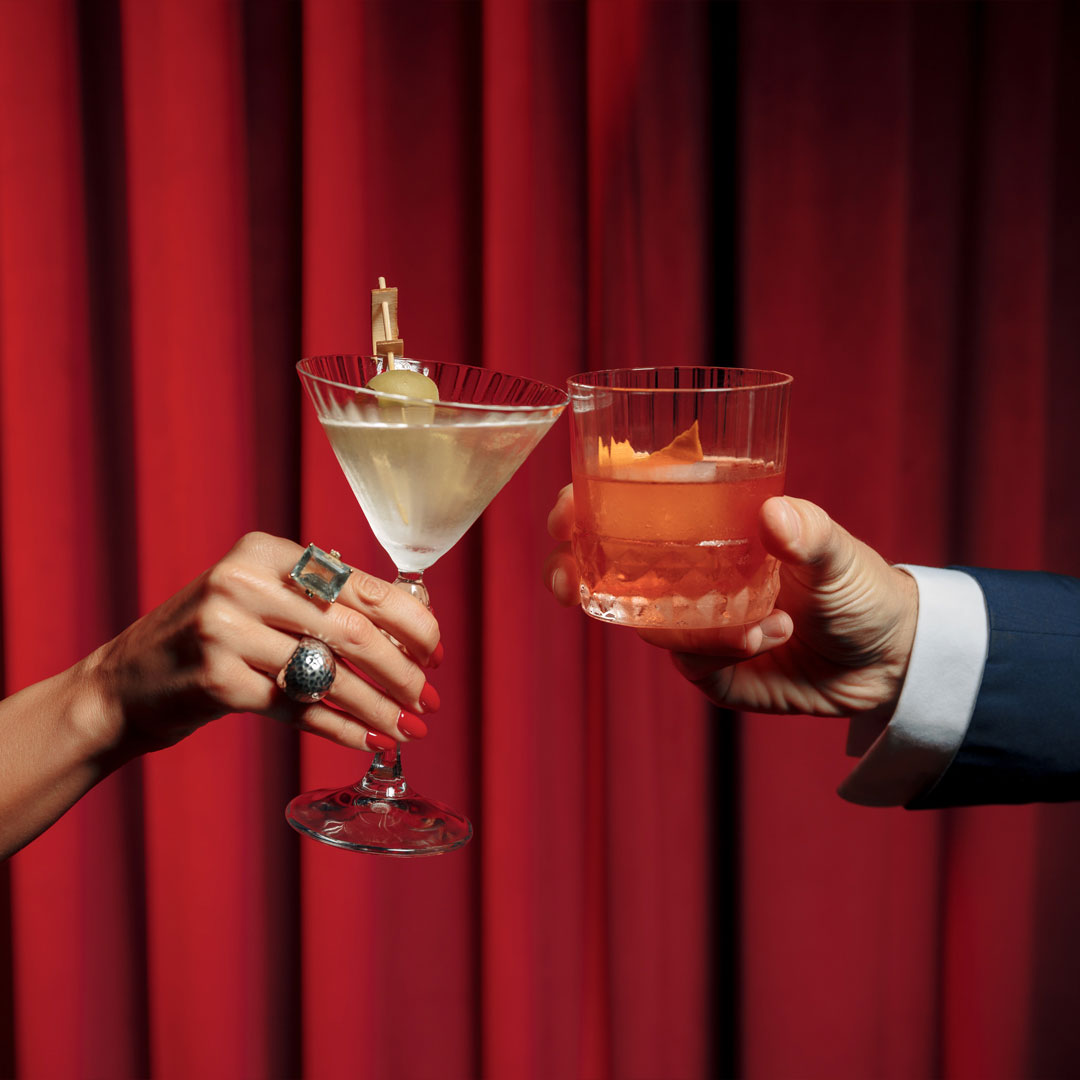 Un brindis con cócteles frente a cortinas rojas